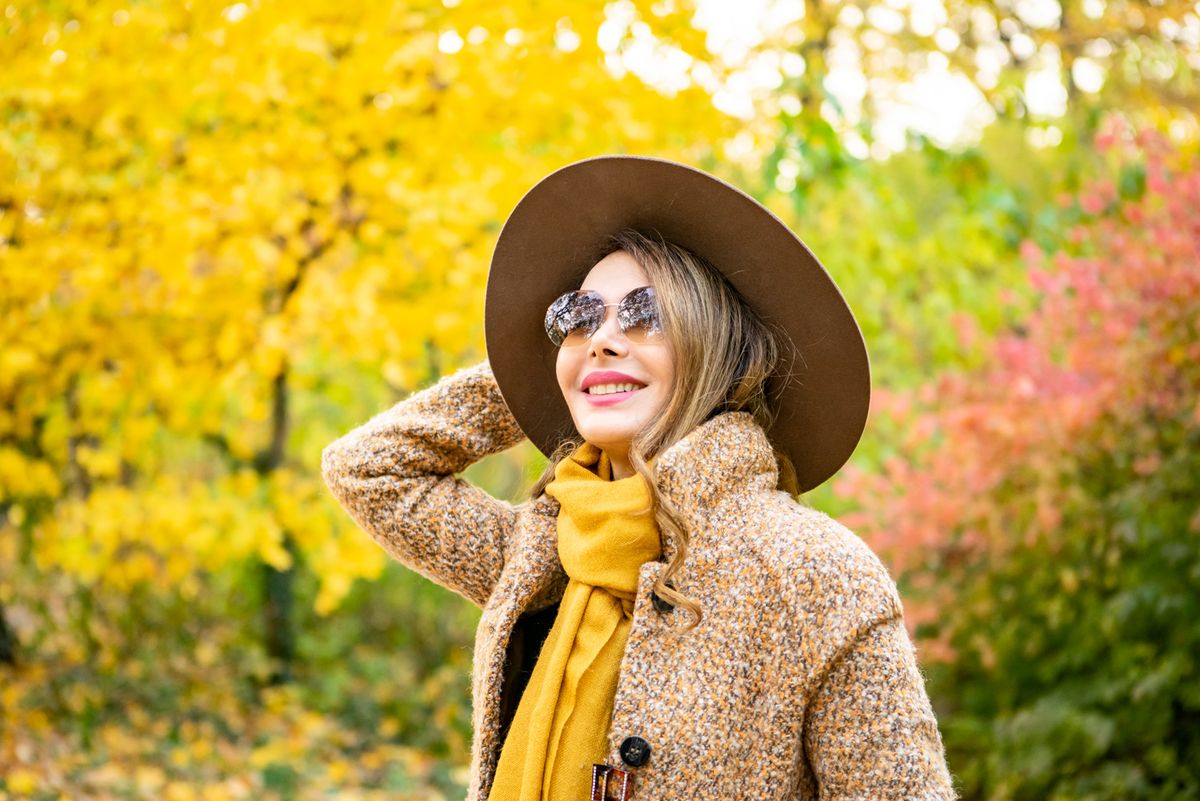 Shiva Boloorian in an autumn park, in a wide-brimmed hat and mustard scarf