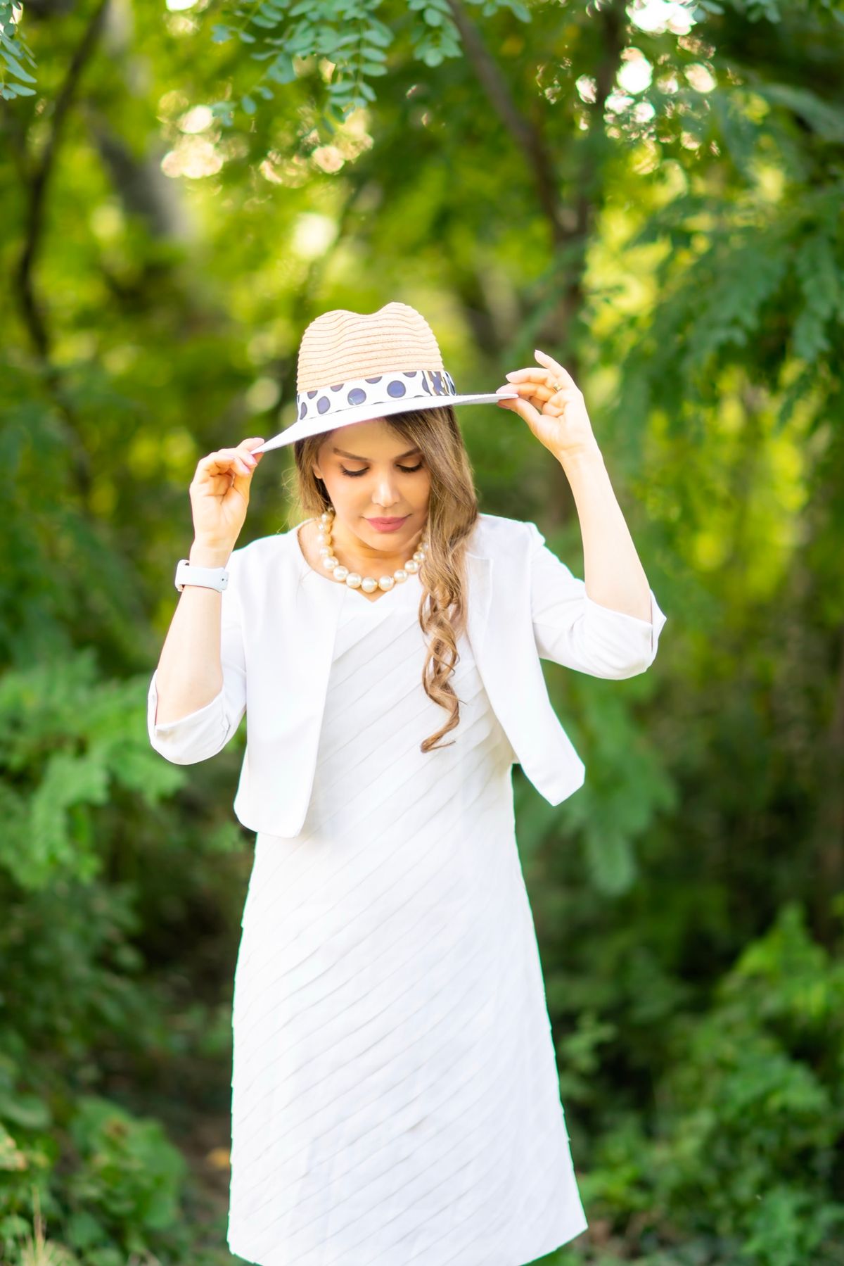 Shiva Boloorian in a white summer dress and hat, in a garden